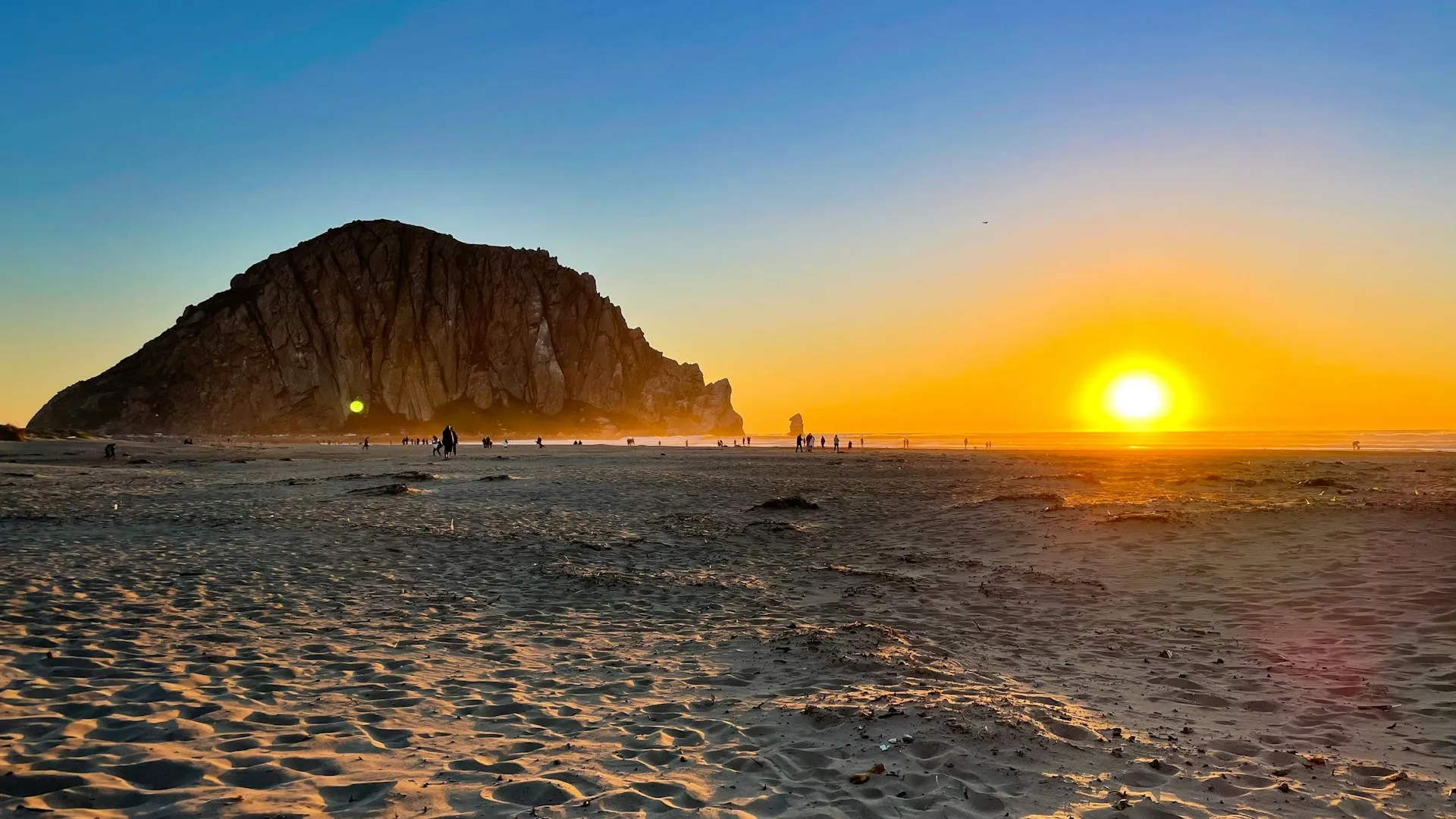 Sunset behind Morro Rock with footprints in the sand on Morro Strand State Beach, San Luis Obispo County.